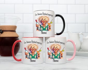 May include: White ceramic mugs with colorful illustrations of a woman holding a bottle and a cocktail. The mugs have black, red, and pink handles and rims. Text on the mugs reads "Das Abenteuer Ruhestand beginnt jetzt" and "Name".