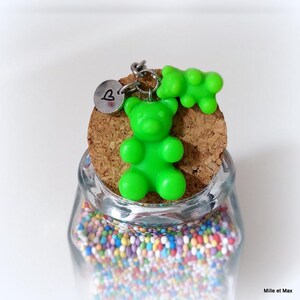May include: A clear glass jar filled with colorful sprinkles, topped with a cork and a green gummy bear keychain. The keychain includes a small silver charm with a heart symbol. The jar is labeled "Mille et Max".