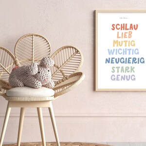 May include: A light pink knitted bunny sits on a white cushioned chair with a woven rattan frame. The chair has a flower-shaped design. A framed print with the text "Ich bin..." and a list of German words in colorful text is on the wall behind the chair.