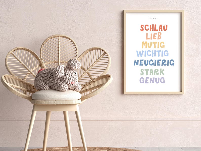 May include: A light pink knitted bunny sits on a white cushioned chair with a woven rattan frame. The chair has a flower-shaped design. A framed print with the text "Ich bin..." and a list of German words in colorful text is on the wall behind the chair.