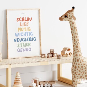 May include: A colorful print with the words "Schlau, Lieb, Mutig, Wichtig, Neugierig, Stark, Genug" in a rainbow color scheme. The print is framed and hanging on a white wall. There is a wooden giraffe toy on a wooden bench in front of the print.