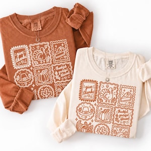 May include: Two long-sleeve shirts, one in rust orange and one in cream, each featuring a grid of white or rust-colored line art illustrations of Thanksgiving icons like a turkey, pumpkin, pie, and hat, with text reading give thanks and thankful grateful blessed.