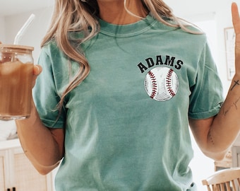 May include: A teal blue t-shirt with the text "ADAMS" in black above a white baseball with red stitching.