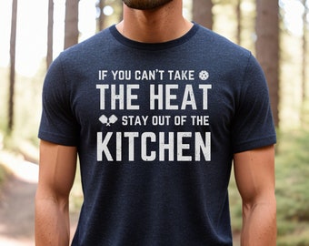 May include: A navy blue t-shirt with white text that reads "If you can't take the heat, stay out of the kitchen". The text is surrounded by images of paddles and a ball, suggesting a sport.
