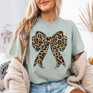 K&ouml;nnte beinhalten: Ein hellgr&uuml;nes T-Shirt mit einem gro&szlig;en Leopardenmuster-Schleifendesign.