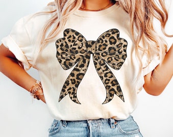May include: A white t-shirt with a large leopard print bow design.