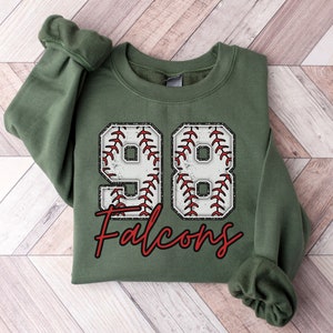 May include: A green sweatshirt with a baseball-themed design. The number 98 is formed using a baseball graphic with red stitching. The text "Falcons" is printed in red below the number.