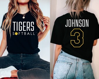 May include: Two black t-shirts. One shirt has the text "TIGERS SOFTBALL" with a yellow softball graphic. The other shirt has the text "JOHNSON" and the number "3" in yellow.