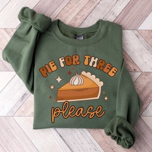 May include: Green sweatshirt with a graphic of a slice of pumpkin pie with the text "Pie for three please" in a retro font.