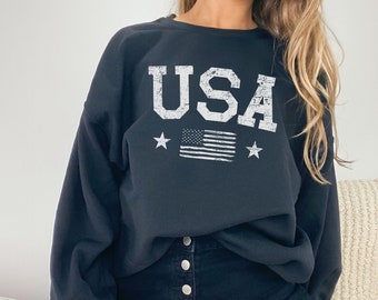 May include: Black sweatshirt with a white distressed graphic of "USA" and a small American flag.