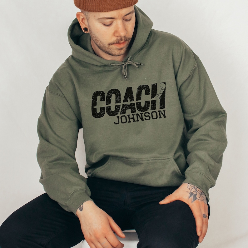 May include: A green hooded sweatshirt with the text "COACH JOHNSON" printed in black with a hockey stick graphic.