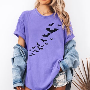 Puede incluir: Una camiseta morada con un gr&aacute;fico de una bandada de murci&eacute;lagos volando en diagonal. Los murci&eacute;lagos son negros y la camiseta es de color morado claro.