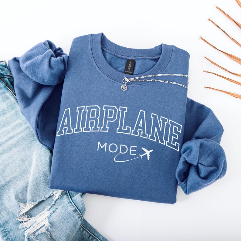 May include: A blue sweatshirt with the text "AIRPLANE MODE" in white with a small airplane graphic. The sweatshirt is folded and laid on a white surface.