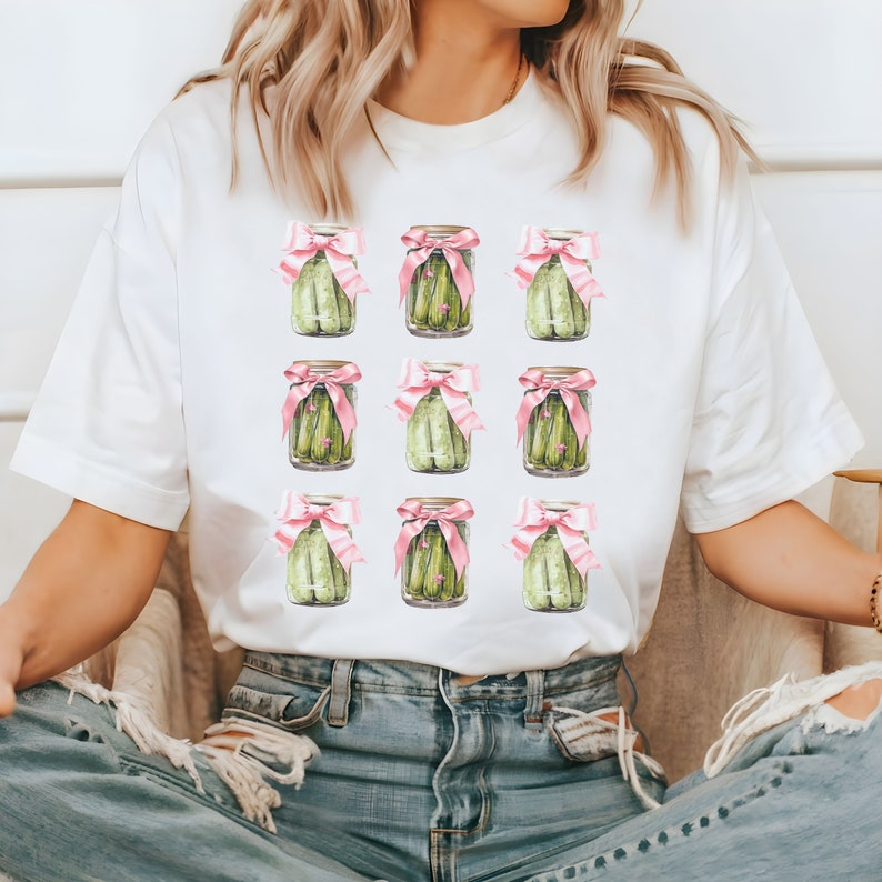 May include: White t-shirt with a repeated pattern of nine jars of pickles tied with pink bows.