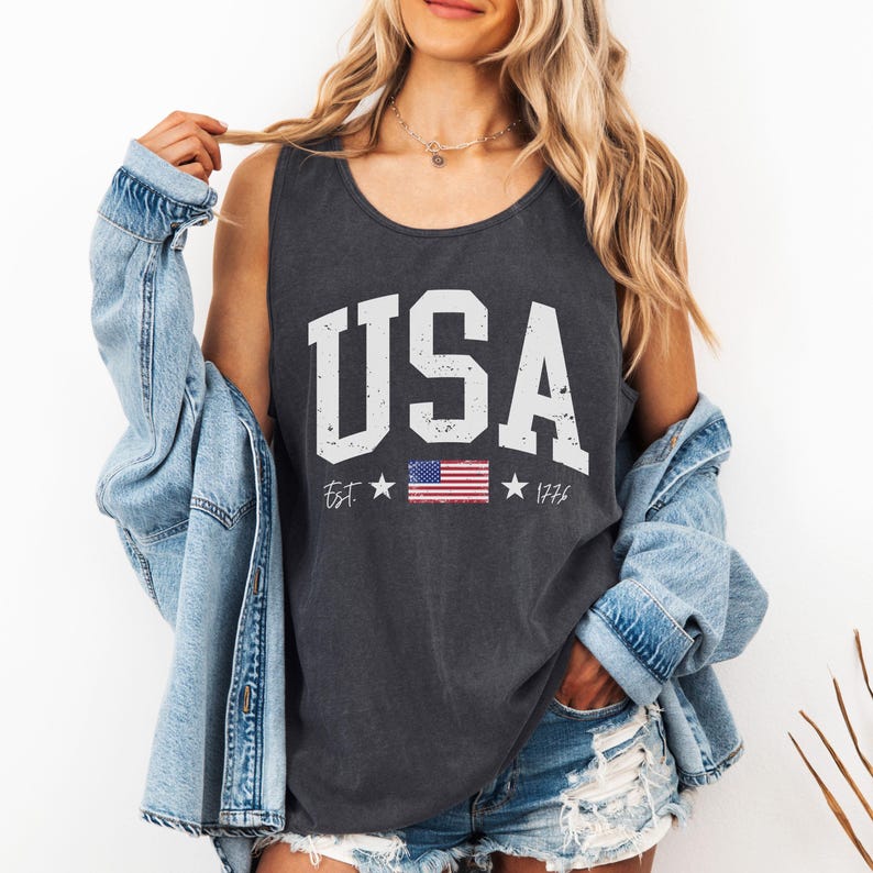 May include: A dark gray sleeveless tank top with a white distressed graphic that says "USA" with a small American flag and the text "Est. 1776".