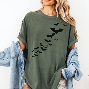Puede incluir: Una camiseta verde con una silueta negra de murci&eacute;lagos volando en diagonal por la parte delantera.