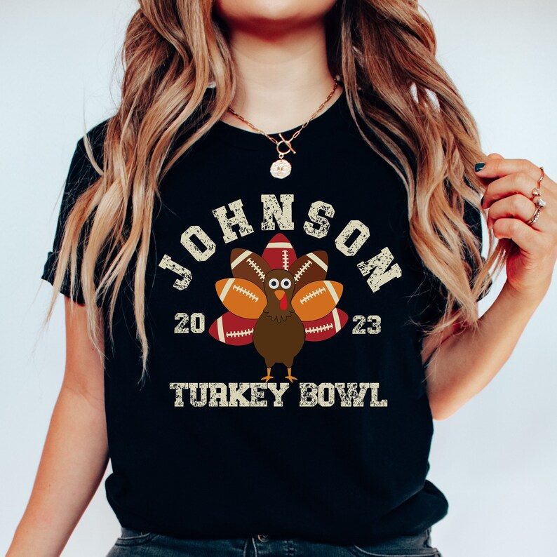 Op de afbeelding: Zwart T-shirt met een vintage-stijl grafische afbeelding van een kalkoen gemaakt van voetballen. De tekst "JOHNSON 20 23 TURKEY BOWL" is op het shirt gedrukt.