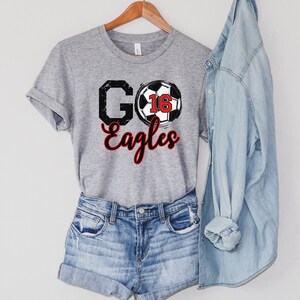 May include: Grey t-shirt with a black and white football graphic and the text "GO Eagles" in black with a red outline.