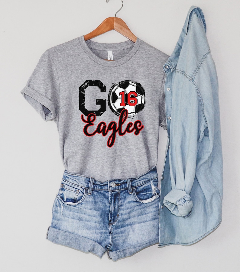 May include: Grey t-shirt with a black and white football graphic and the text "GO Eagles" in black with a red outline.