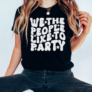 May include: Black t-shirt with white text that reads "WE*THE PEOPLE*LIKE*TO PARTY" in a retro font with stars.