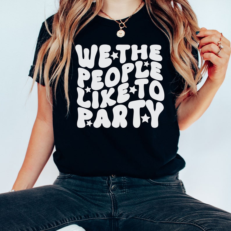 May include: Black t-shirt with white text that reads "WE*THE PEOPLE*LIKE*TO PARTY" in a retro font with stars.