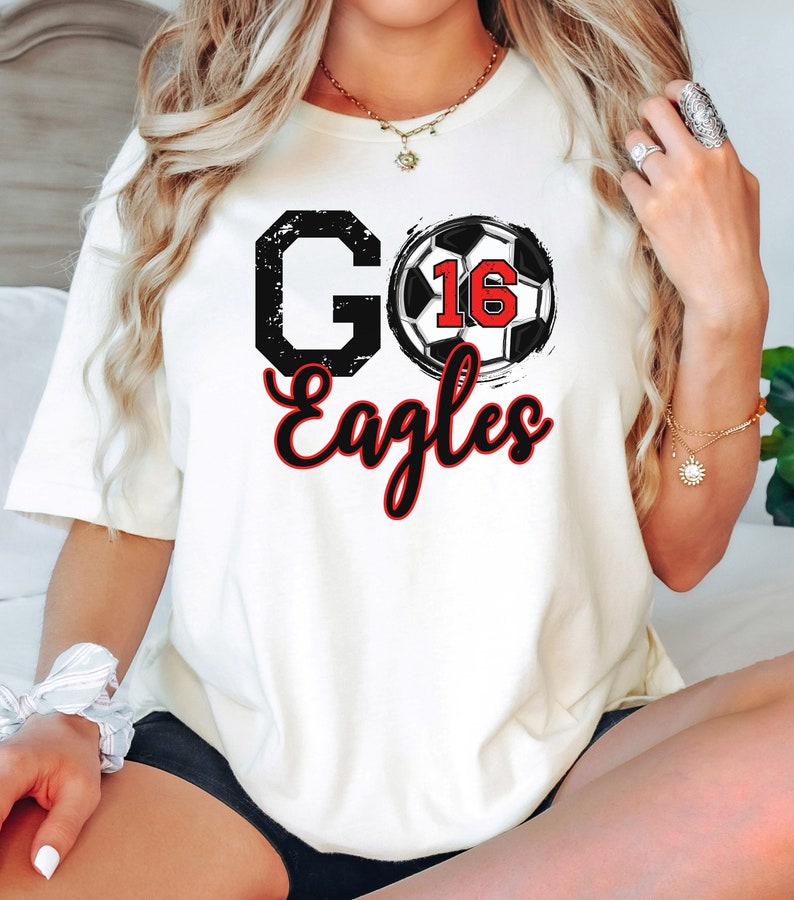 May include: White t-shirt with a black and white football graphic and the text "GO Eagles" in red and black.