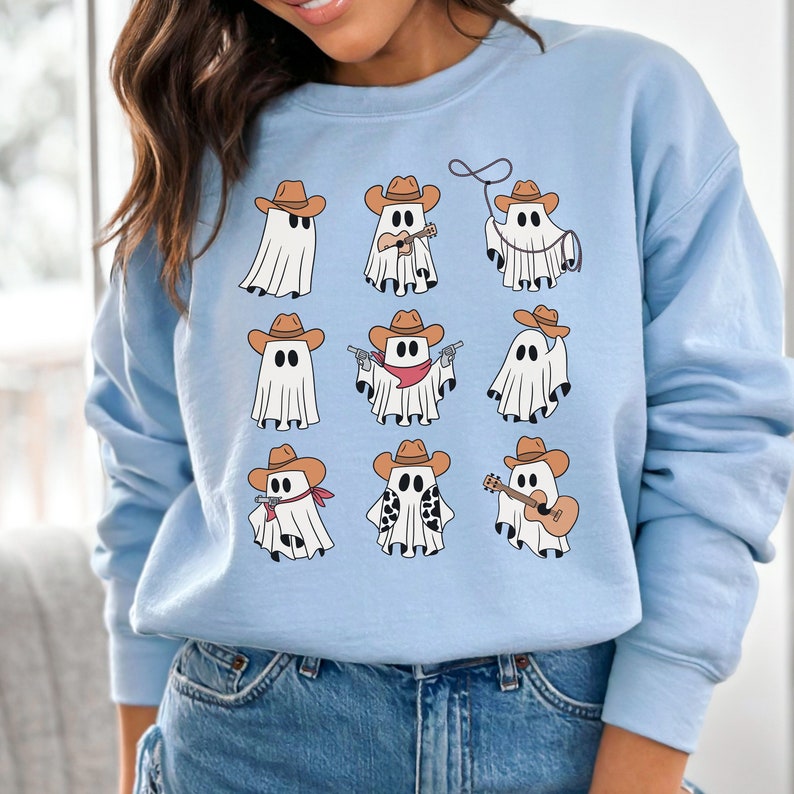 May include: Light blue sweatshirt with a graphic of nine cartoon ghosts wearing cowboy hats and doing various activities. The ghosts are wearing brown cowboy hats, red bandanas, and holding instruments like a guitar and ukulele.
