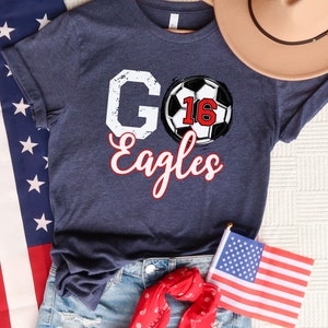May include: A navy blue t-shirt with a white graphic of a football with the number 16 and the words "Go Eagles" in red and white.