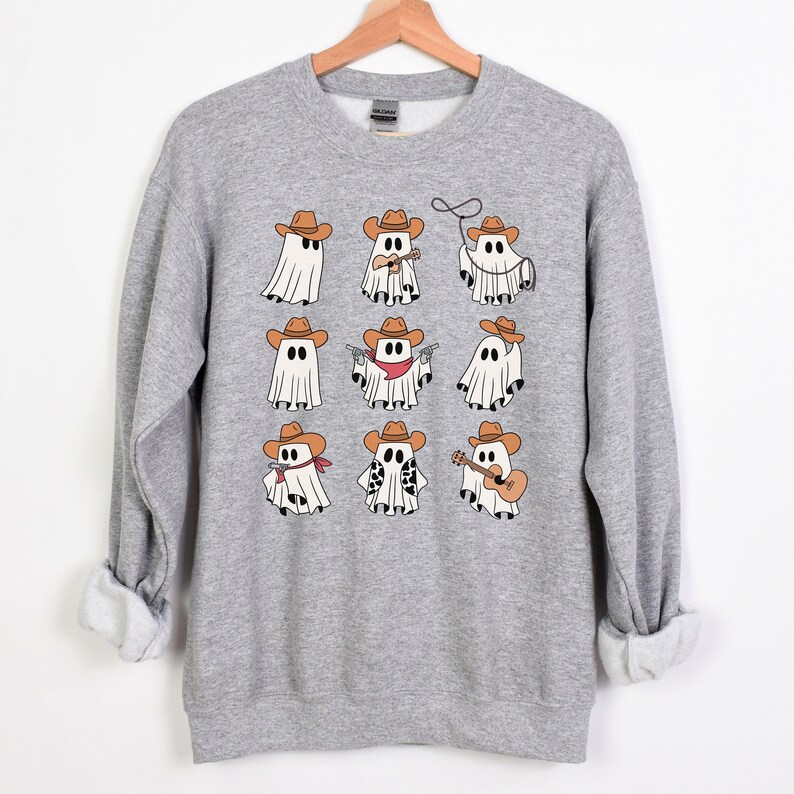 May include: A gray sweatshirt with a design of nine cartoon ghosts wearing cowboy hats and various accessories, including a lasso, a guitar, and a gun.
