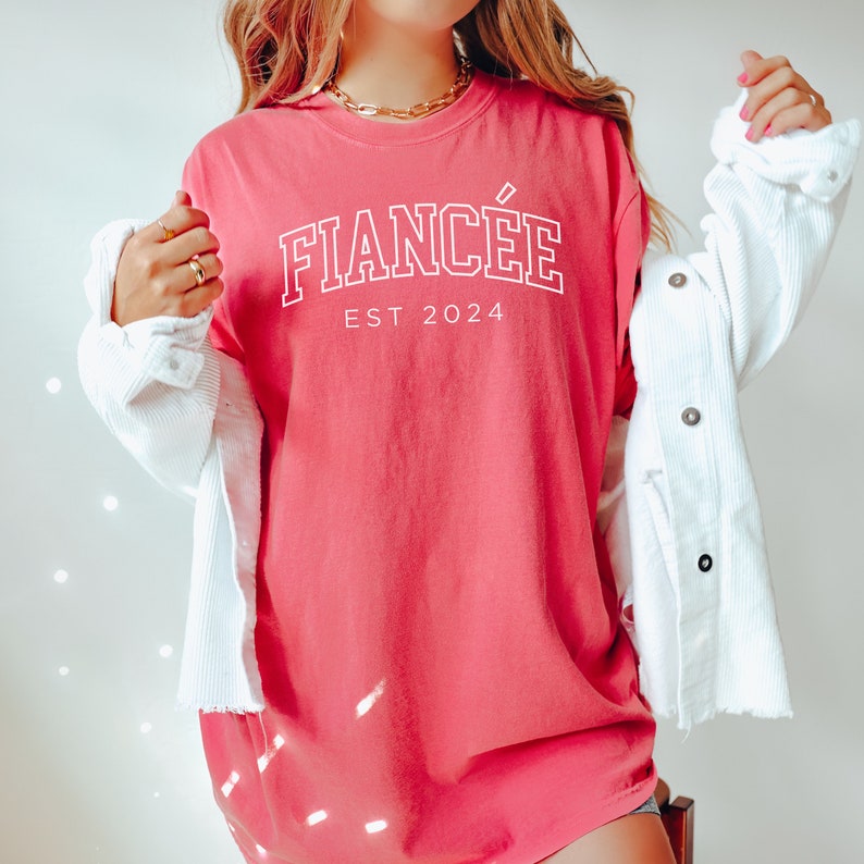 Puede incluir: Una camiseta rosa con el texto "FIANC&Eacute;E EST 2024" en blanco.