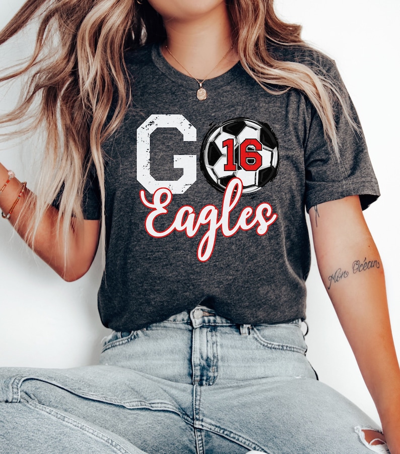 May include: A dark grey t-shirt with a white distressed "GO" and "Eagles" in red script. A black and white football with the number "16" in red is centred between the words.