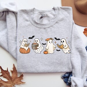 Puede incluir: Sudadera gris claro con un dise&ntilde;o tem&aacute;tico de Halloween. El dise&ntilde;o incluye cuatro fantasmas de dibujos animados leyendo libros, con calabazas, murci&eacute;lagos y estrellas. La sudadera est&aacute; hecha de un material suave.