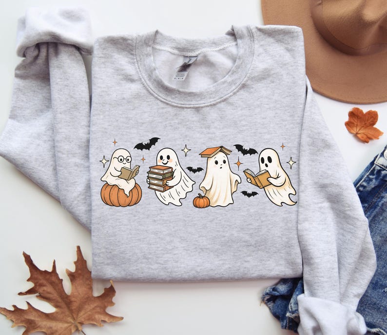 Puede incluir: Sudadera gris claro con un dise&ntilde;o tem&aacute;tico de Halloween. El dise&ntilde;o incluye cuatro fantasmas de dibujos animados leyendo libros, con calabazas, murci&eacute;lagos y estrellas. La sudadera est&aacute; hecha de un material suave.
