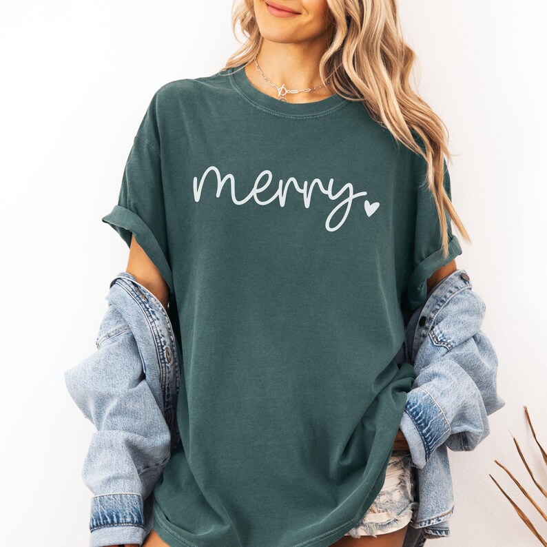 May include: A teal green t-shirt with the word "merry" written in white cursive with a small white heart next to it.