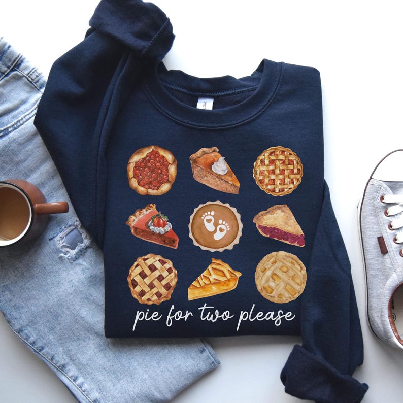 May include: A navy blue sweatshirt with a graphic of various pies, including cherry, pumpkin, apple, and pecan. The text "pie for two please" is printed below the pies.
