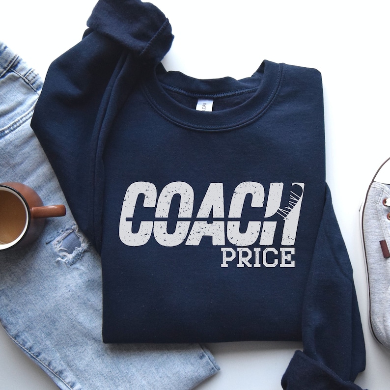 May include: Navy blue sweatshirt with white text that reads "COACH PRICE" with a hockey stick graphic.