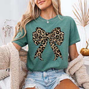 K&ouml;nnte beinhalten: Ein tealgr&uuml;nes T-Shirt mit einem gro&szlig;en Leopardenmuster-Schleifendesign.