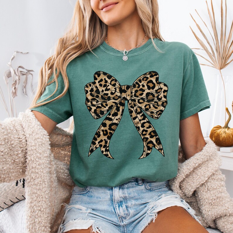 K&ouml;nnte beinhalten: Ein tealgr&uuml;nes T-Shirt mit einem gro&szlig;en Leopardenmuster-Schleifendesign.