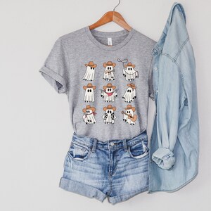 May include: A gray t-shirt with a design of nine white ghosts wearing cowboy hats and various accessories. The ghosts are playing instruments, holding guns, and lassoing.