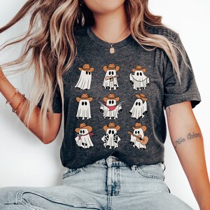 May include: A dark gray t-shirt with a graphic of nine cartoon ghosts wearing cowboy hats. The ghosts are doing different activities, such as playing guitar, holding a gun, and wearing a bandana. The text "More Ocean" is written on the right sleeve of the shirt.