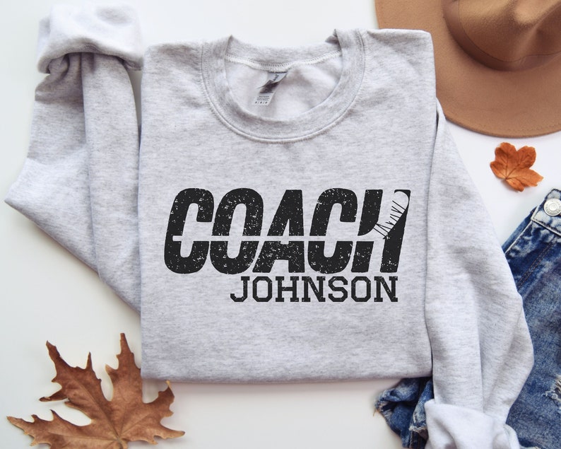 May include: Grey sweatshirt with black text that reads "COACH JOHNSON" with a hockey stick graphic.