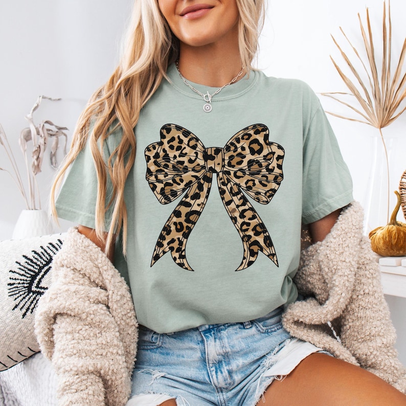 K&ouml;nnte beinhalten: Ein hellgr&uuml;nes T-Shirt mit einem gro&szlig;en Leopardenmuster-Schleifendesign.