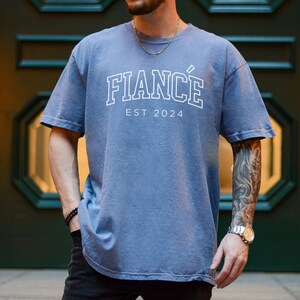 Puede incluir: Una camiseta azul con un gr&aacute;fico blanco que dice "FIANC&Eacute;" y "EST 2024".