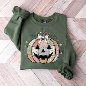 Peut inclure: Sweat-shirt vert avec un motif citrouille patchwork, un nœud blanc, des cœurs et des détails floraux. La citrouille a un visage de Jack-o'-lantern. Un haut de saison confortable pour l'automne et Halloween.