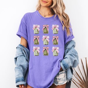 May include: Purple t-shirt with a repeated pattern of pickle jars tied with pink bows.