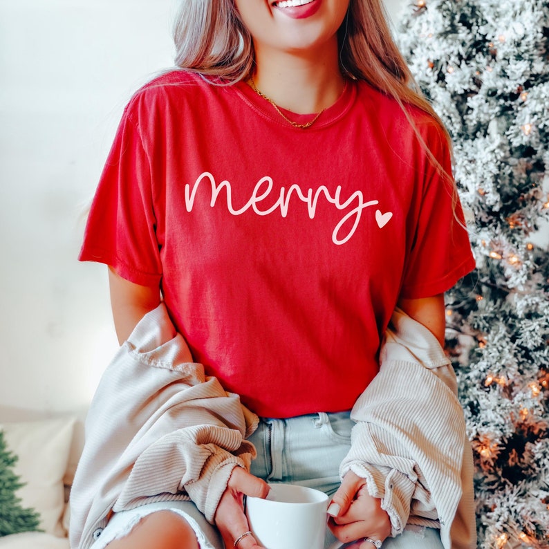 May include: Red t-shirt with the word "merry" in white script with a small pink heart.
