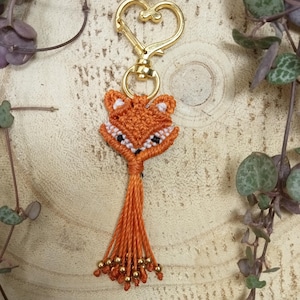 Peut inclure: Un porte-clés renard orange fait à la main avec un fermoir doré en forme de cœur. Le renard est fabriqué avec des nœuds macramé, avec des accents blancs et des yeux noirs. Le porte-clés a une gland de fils orange avec des perles dorées.