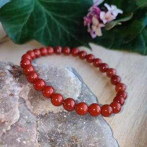 Op de afbeelding: Rode edelsteen armband met ronde kralen. De armband ligt op een witte en grijze steen.