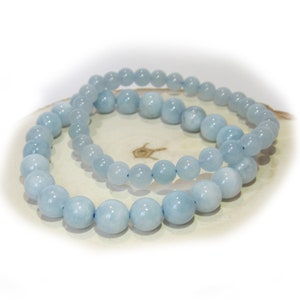 Pode incluir: Duas pulseiras de contas de água-marinha azul claro empilhadas uma em cima da outra. As pulseiras são feitas de contas redondas e estão sobre uma superfície de madeira.