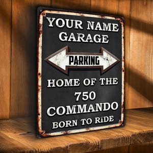 May include: A rectangular black metal sign with white text and a brown arrow design. The sign reads "YOUR NAME GARAGE PARKING HOME OF THE 750 COMMANDO BORN TO RIDE". The sign has a distressed, vintage look with rusty edges.